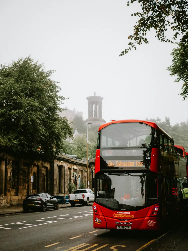 A red City Sightseeing bus with Calton Hill behind
